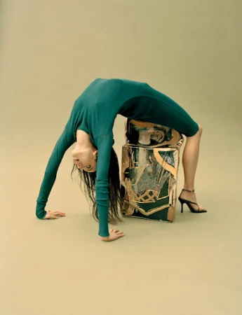 Model in a green ribbed dress bending backward in a bridge pose over a metallic patterned block