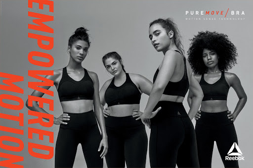 Four diverse women pose in black athletic wear against a gray background. Empowered Motion text, Reebok logo, and PureMove Bra branding.