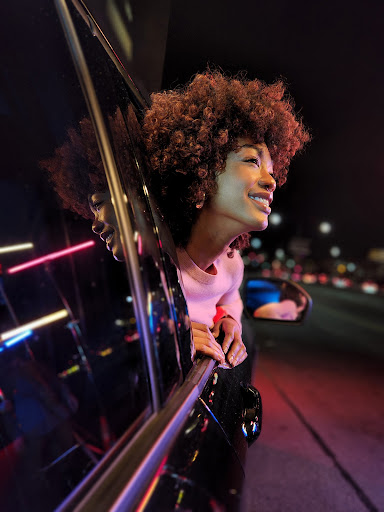 Portrait of an African-American woman smiling out of a car window at night, with city lights blurred in the background.