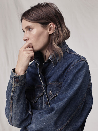 Woman in a denim jacket with her fingers to her mouth in a close-up studio shot, showcasing a casual and contemplative fashion image.
