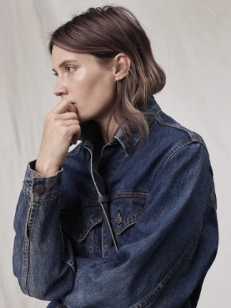 Woman in a denim jacket with her fingers to her mouth in a close-up studio shot, showcasing a casual and contemplative fashion image.