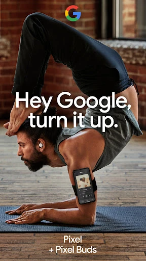 Man in handstand wearing wireless earbuds and a smartphone armband on a yoga mat in a room with a brick wall.