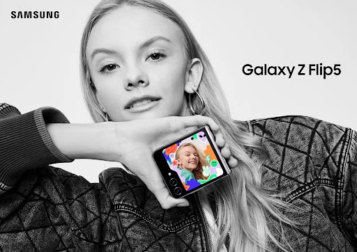 Monochrome studio shot of a smiling young woman holding up a foldable smartphone showcasing a video call, promoting mobile technology.