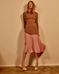 Model wearing a brown knit sweater and pink pleated skirt standing against a neutral wall