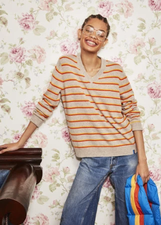Smiling model wearing striped sweater and glasses standing against pink floral wallpaper holding puffer jacket