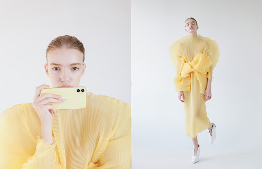 Woman in yellow dress holds a yellow smartphone in a full studio shot with a white background, showcasing a modern fashion aesthetic.