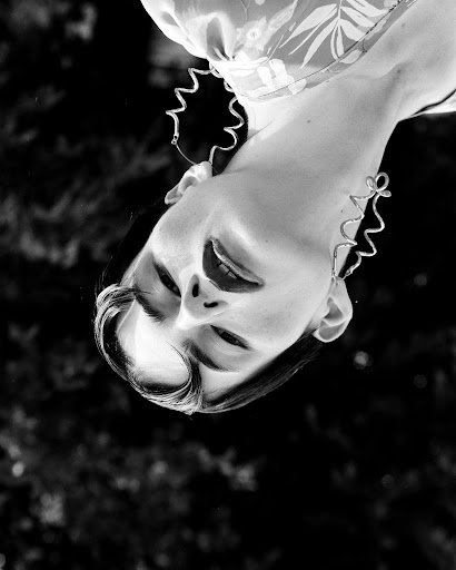 Monochrome portrait of a woman wearing large wavy hoop earrings and a patterned top, shot from an inverted angle.