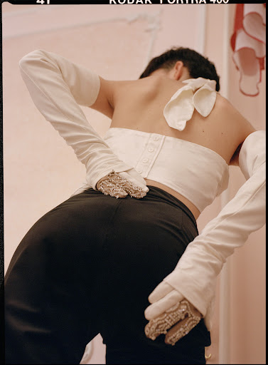 Back view of person in black pants and white top and long gloves, close-up studio shot showing detailed fashion style and neutral background.