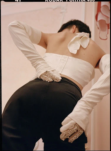 Back view of person in black pants and white top and long gloves, close-up studio shot showing detailed fashion style and neutral background.