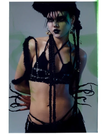 Model with avant-garde dark makeup and braided hair wearing a black strapped top and fuzzy headpiece