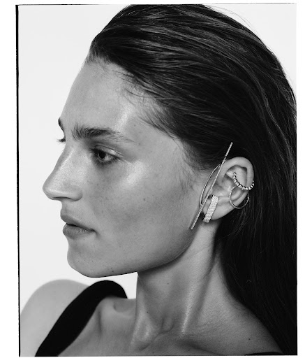 Profile portrait of a woman with wet hair wearing sculptural silver ear cuffs and earrings against a plain white background