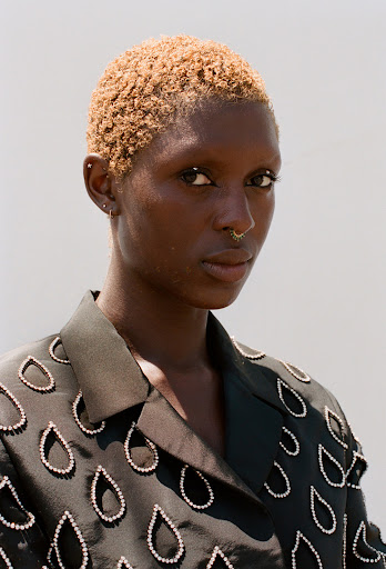 Close-up studio shot of an African woman with short blonde hair, wearing a designer black jacket with water drop design.