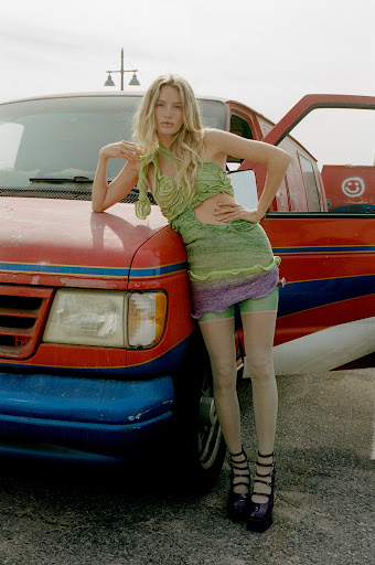 Fashionable woman posing with a vintage red van in a stylish green knit dress and platform shoes against a clear sky.