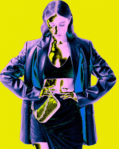 A woman in a black crop top and skirt, with a blue blazer and a small bag, poses in front of a yellow background in a fashion style image.