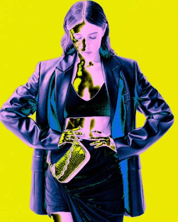A woman in a black crop top and skirt, with a blue blazer and a small bag, poses in front of a yellow background in a fashion style image.
