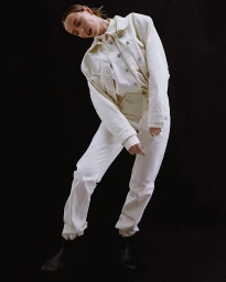 Model in white denim jacket and trousers posing against a dark background, styled by Mari Siviakova.