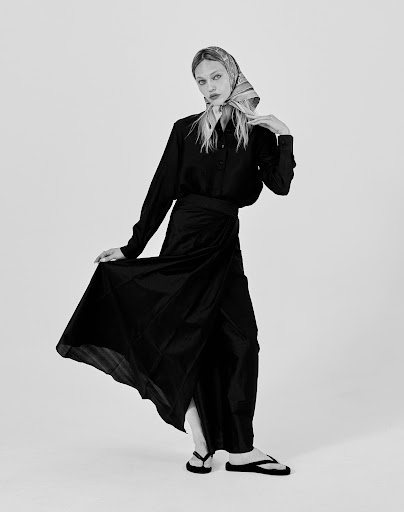 Model wearing a black long-sleeve shirt, long skirt, and patterned headscarf against a light background.