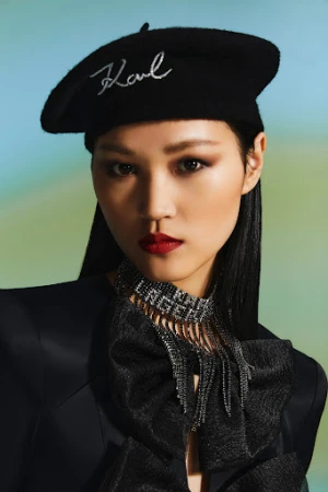 Close-up portrait of an East Asian woman wearing a black beret, dark blazer, and elaborate rhinestone collar necklace styled by Ruben De Melo Moreira.