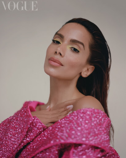 Close-up studio portrait of a woman with yellow eyeshadow wearing a pink sequined top, looking at the camera with neutral expression.