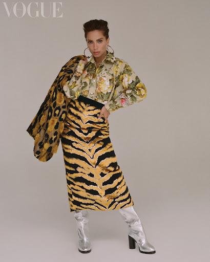 Editorial fashion shot of a woman in patterned shirt and tiger print skirt with hoop earrings and silver boots standing in a photo studio.