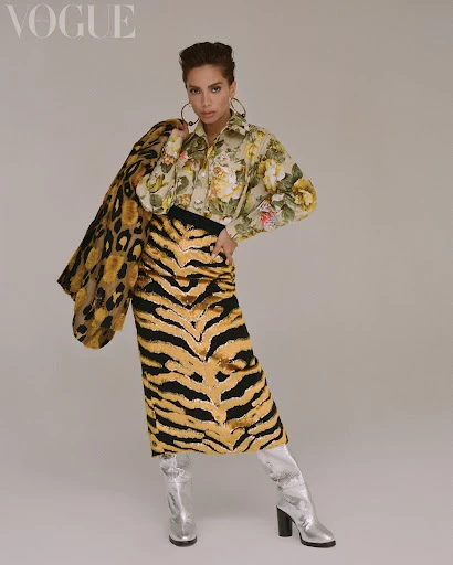 Editorial fashion shot of a woman in patterned shirt and tiger print skirt with hoop earrings and silver boots standing in a photo studio.