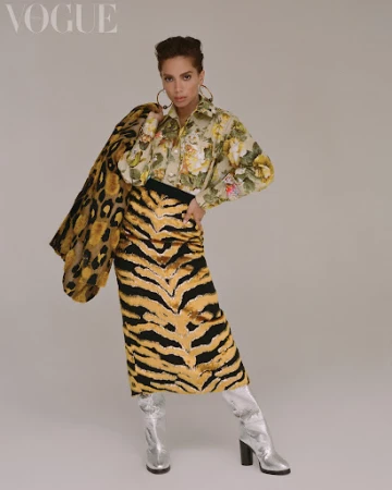 Editorial fashion shot of a woman in patterned shirt and tiger print skirt with hoop earrings and silver boots standing in a photo studio.
