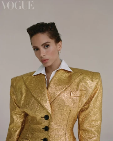 Portrait of woman in a gold, shimmering blazer with a white collared shirt underneath against a neutral background.