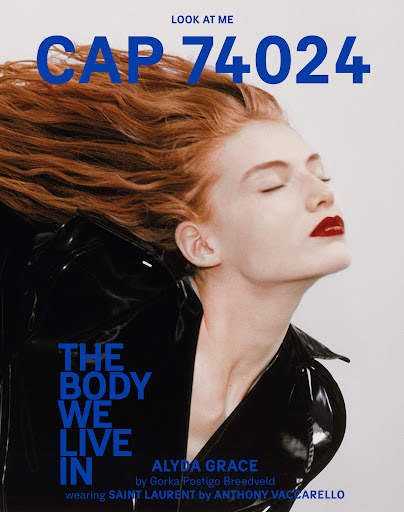 Fashion editorial shot: Portrait of a model with auburn hair and glossy red lips wearing a patent leather jacket, set against a light background.