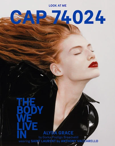 Fashion editorial shot: Portrait of a model with auburn hair and glossy red lips wearing a patent leather jacket, set against a light background.