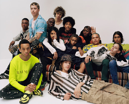 Group portrait of casually dressed young adults posing on a striped sofa in a studio setting, showcasing diverse styles and expressions.