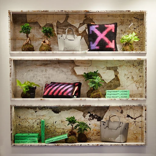 Shelves display handbags, decorative pillows with arrow design, and potted plants in a retail environment with unique backdrop.