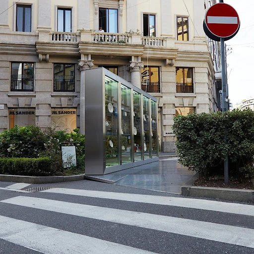 Modern glass bus stop shelter in urban setting against a building facade, with a pedestrian crosswalk in the foreground.
