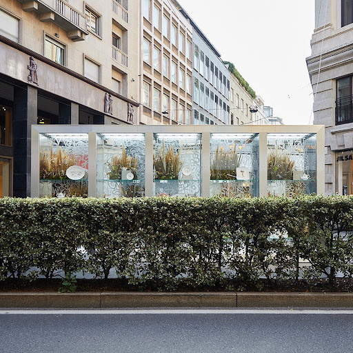 Urban retail storefront display with floral arrangements behind glass panels, framed by modern architecture in an Italian city street.