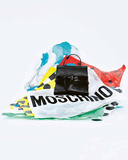 Black leather handbag on a pile of branded shopping bags against a white backdrop, creating a high-fashion editorial image.