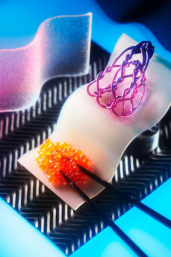 Artistic still life: orange caviar on a white surface with metal accents, illuminated by neon blue and pink lighting, creating a surreal scene.