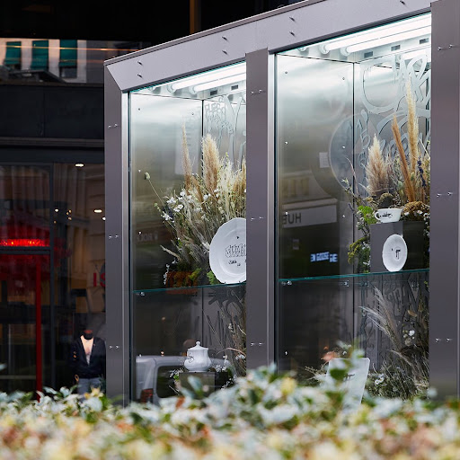 Modern glass display showcase featuring white ceramic tableware and dried pampas grass arrangements designed by Alessandro Mensi.