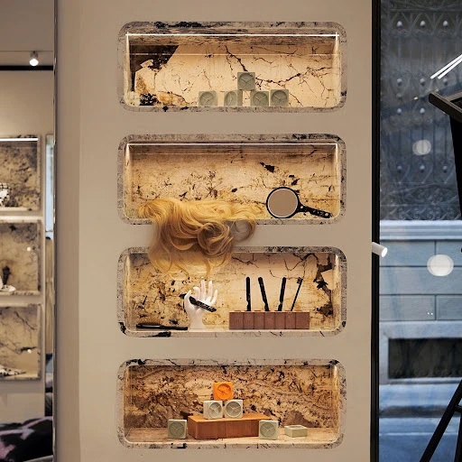 Display shelves hold clocks, hair extensions, and makeup tools against a marble backdrop in a retail setting with neutral lighting.
