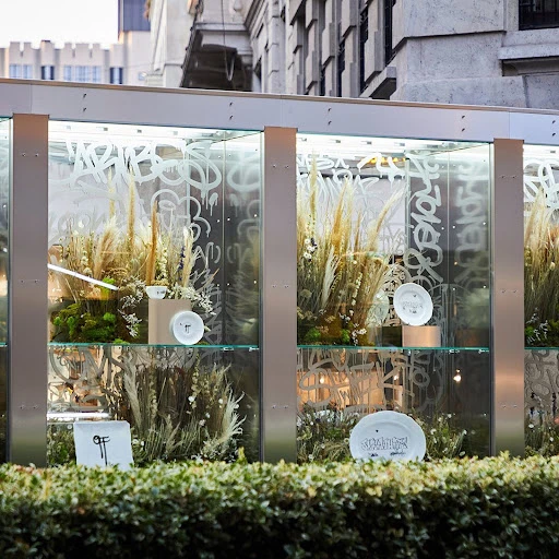 Retail display window featuring botanical arrangements and ceramic plates with graffiti etched glass.