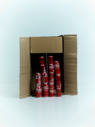 Several red and white Coca-Cola cans are stacked within a cardboard box against a white background, product shot, soda, drink, beverage.