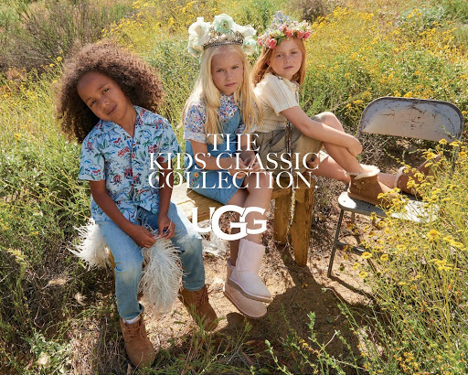 Three children wearing floral crowns and casual apparel outdoors in a grassy field with sheepskin boots.