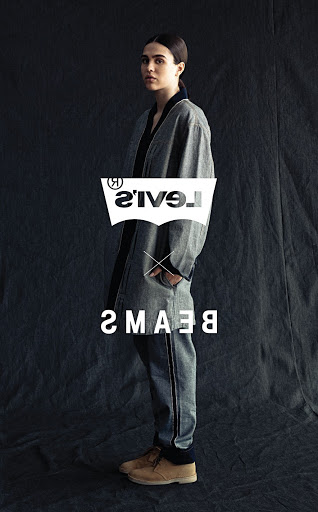 Woman wearing a gray jacket and pants with tan shoes, posing in front of a dark gray background, with Levi's and BEAMS logos displayed.