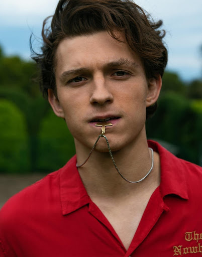 Close-up portrait of a young man with dark hair wearing a red collared shirt and a unique golden accessory attached to his lip.