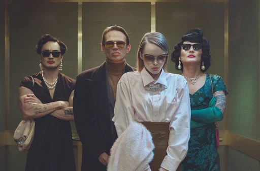 Four people standing together in an elevator wearing sunglasses and vintage-inspired clothing, designed by Ariana Nakata.