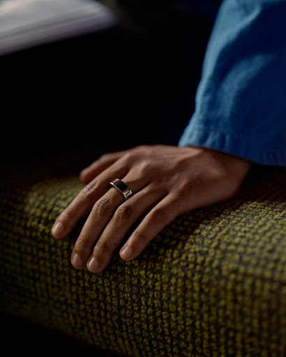 Close-up of a hand wearing a ring resting on a textured green surface, capturing details of the hand, ring, and textile.