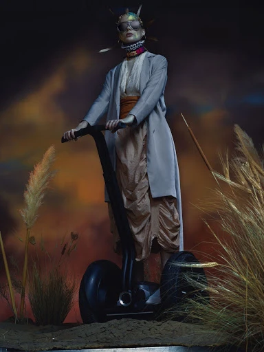 Person wearing sunglasses on a Segway, standing outdoors surrounded by tall wheat grass, with a cloudy, orange and blue-toned background.