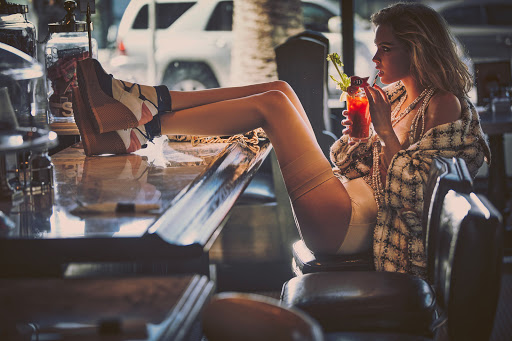 Stylish woman relaxes in retro diner booth, legs propped on the counter, sipping a Bloody Mary cocktail and adorned in pearls and tweed.