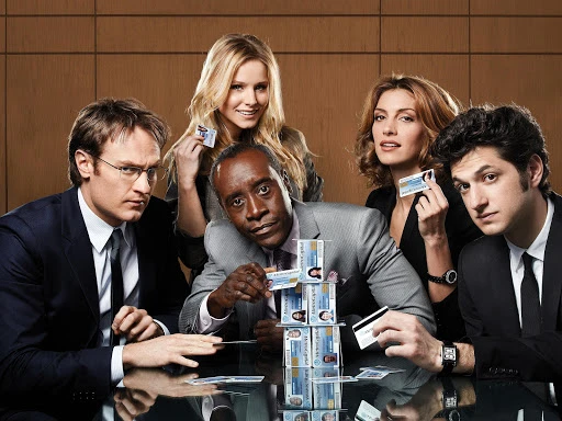 Group portrait of five smiling adult men and women at a table with a house of cards made from ID cards on a reflective table.