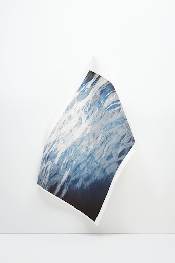 Abstract studio shot of a photograph depicting ocean waves, displayed against a neutral white wall and surface in a minimalist setting.