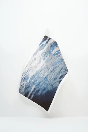 Abstract studio shot of a photograph depicting ocean waves, displayed against a neutral white wall and surface in a minimalist setting.