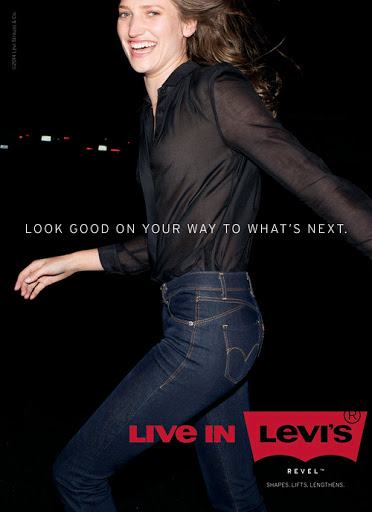 Smiling woman wearing a black sheer shirt and blue denim jeans against a dark night background with red Levi's branding.